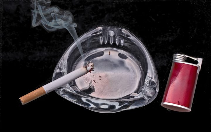 Brandende sigaret in een glazen asbak naast een aansteker